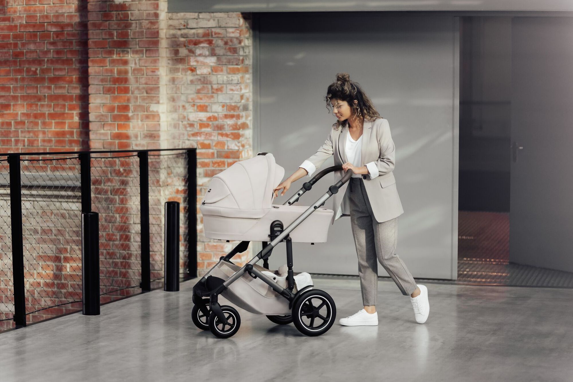 Parent pushing a SMILE 5Z stroller with a carrycot, gently checking on the baby.
